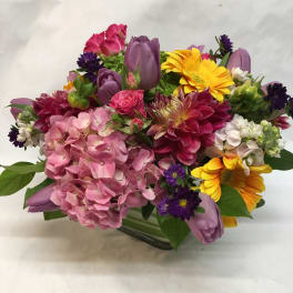 Mixed bouquet with pink hydrangea, purple tulips, and yellow daisies in a glass vase