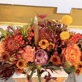 Autumn floral centerpiece with orange blooms and red berries around a candle