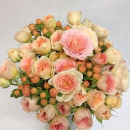 Bouquet of blush roses and peach ranunculus in a woven vase