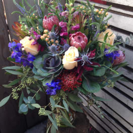 Mixed bouquet with protea, roses, and blue flowers in a glass vase