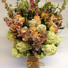 Tall mixed bouquet in a burlap-wrapped vase with peach, pink, and green blooms