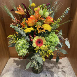 Tall mixed bouquet in a glass vase with orange roses and lilies