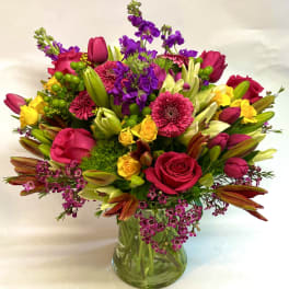 Mixed bouquet of pink, purple, and yellow flowers in a glass vase