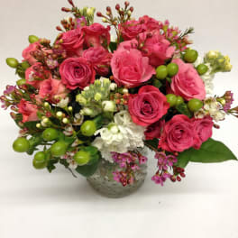 Pink rose bouquet in a textured glass vase with white blooms and green berries
