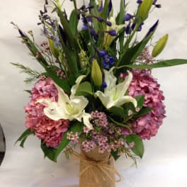 Bouquet of pink hydrangeas, white lilies, and purple flowers in a burlap-wrapped vase