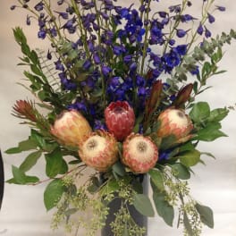 Tall bouquet with blue delphinium and pink protea in a black vase