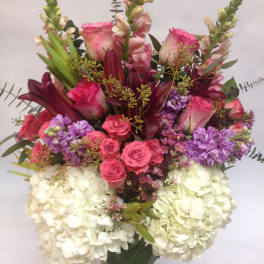 Mixed bouquet of pink roses, purple flowers, and white hydrangeas in a glass vase