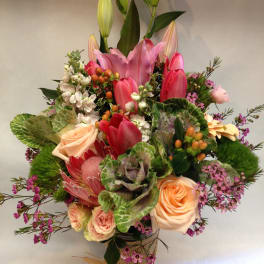 Mixed bouquet with pink lilies, roses, and tulips in a wrapped vase