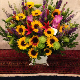 Large mixed bouquet with sunflowers, lilies, and purple flowers in a white container