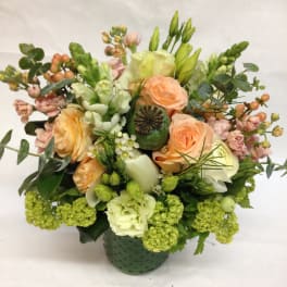 Mixed bouquet of peach roses, white blooms, and green flowers in a green vase