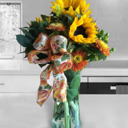 Sunflower bouquet with orange mums and a patterned ribbon in a glass vase