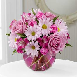 Pink roses and daisies arranged in a round glass vase