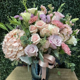 Pastel bouquet of roses, hydrangea, and lisianthus in a blue vase with ribbon