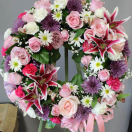 Standing wreath of pink roses, lilies, white daisies, carnations, and purple mums with a pink ribbon on an easel