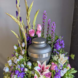 Floral urn arrangement with pink lilies and roses around a gray cremation urn