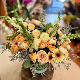 Low floral arrangement of peach roses and pale yellow blooms in a vase