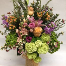 Mixed bouquet with roses, lilies, hydrangeas, and berries in a burlap-wrapped vase