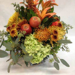 Orange lilies and chrysanthemums with apples in a glass vase