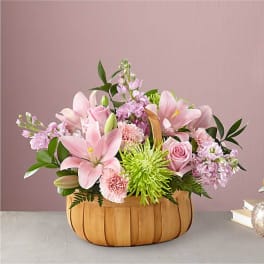 Pink lilies and roses in a wooden basket with green accents