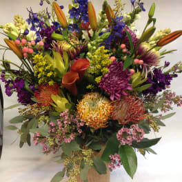Mixed bouquet with lilies, calla lilies, and purple blooms in a burlap-wrapped vase