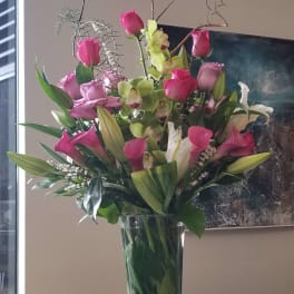 Tall bouquet of pink roses, calla lilies, and green orchids in a glass vase
