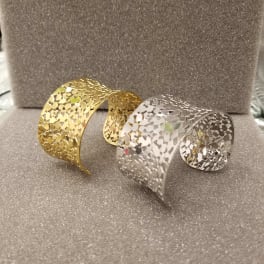 Two decorative metal cuff bracelets on a glittery gray surface