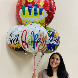 Smiling woman holding a cluster of colorful round Happy Birthday balloons.