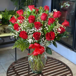 Red roses arranged in a clear glass vase with baby's breath and a red ribbon