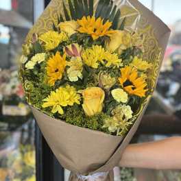 Yellow mixed bouquet wrapped in brown paper with a ribbon