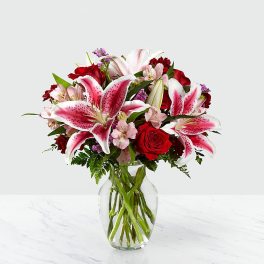 Bouquet of pink lilies and red roses in a clear glass vase