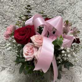 Pink and red roses in a glass vase with a pink ribbon