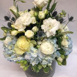 White and pale blue floral arrangement in a gray vase
