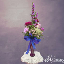 Purple and pink floral arrangement in a tall vase with a blue ribbon