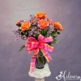 Orange roses in a glass vase with a pink plaid ribbon