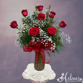 Red roses in a glass vase with baby's breath and a red ribbon