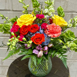 Colorful bouquet of roses, carnations, and other blooms in a textured glass vase