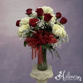 Red roses and white hydrangeas in a glass vase with a red ribbon