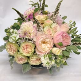 Pastel bouquet of roses, dahlias, and white flowers in a low container