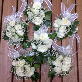 White rose corsages with ribbon bows on a wooden surface