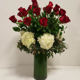 Tall arrangement of red roses and white hydrangeas in a clear green-lined glass vase