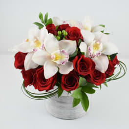 Round arrangement of white orchids and red roses in a low white cylinder vase