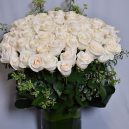 Large arrangement of ivory roses with decorative foliage in a clear glass cylinder vase.