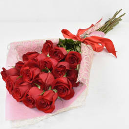 Hand-tied bouquet of long-stem red roses wrapped in pink lace paper with a red ribbon bow