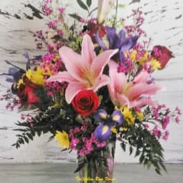 Tall mixed bouquet with pink lilies, a red rose, and purple flowers in a glass vase