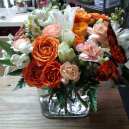 Orange and peach rose bouquet in a clear glass vase with white lilies