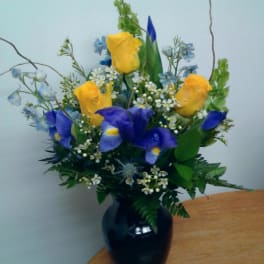 Yellow roses and blue irises in a black vase