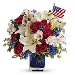 Red roses and white lilies in a blue vase with a small American flag