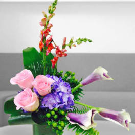Pink roses, purple hydrangea, and calla lilies in a green vase