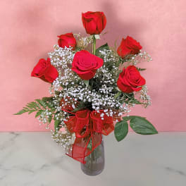 Red roses in a glass vase with baby's breath and a red ribbon