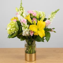 Bouquet of yellow lilies, pink roses, and white blooms in a glass vase